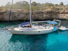 A lively group enjoys a day on a sailboat anchored in crystal-clear waters, perfect for swimming and relaxation amidst stunning coastal scenery.