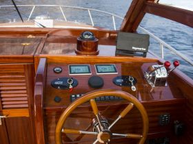 A detailed view of the helm and console of a boat, showcasing the elegant wooden finish and navigational instruments, perfect for a luxurious boating experience.