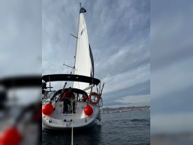A scenic view of a sailing boat with crew members on board, navigating the ocean with a city skyline in the background — perfect for showcasing sailing adventures.