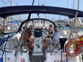 A group of friends relaxes inside the helm of a sailboat, enjoying the sunny weather and the marina view — perfect for a day out on the water.