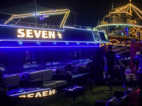 A stylish interior of a boat named 'Seven' featuring modern lounge seating and ambient lighting, perfect for evening gatherings and celebrations on the water.