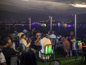 A lively group enjoys a night out on a boat, dining and socializing against the backdrop of a vibrant city skyline — perfect for memorable celebrations and gatherings.