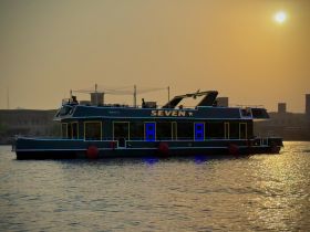 A stunning yacht named 'Seven' glides through the water at sunset, showcasing its elegant design and vibrant lighting — perfect for evening cruises.