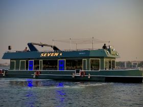 A stunning view of the 'SEVEN' yacht, showcasing its sleek design and vibrant lighting as it navigates the water, perfect for luxurious outings.