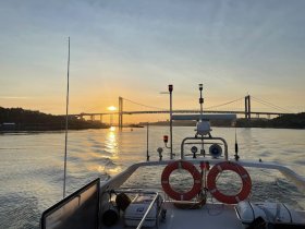 A serene sunset view from the deck of a boat, showcasing a bridge in the background and the shimmering water, perfect for capturing the beauty of evening cruises.