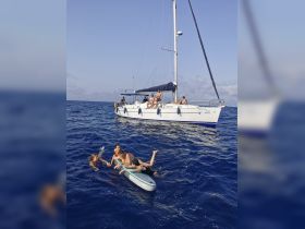 A fun-filled day on the water with kids enjoying paddleboarding and swimming near a sailboat, capturing the essence of summer adventures at sea.