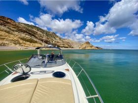 A couple enjoys the stunning coastal views from their boat, surrounded by picturesque cliffs and clear waters — a perfect getaway for nature lovers.