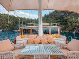 A beautifully designed lounge area on a yacht, featuring comfortable seating and a glass table, perfect for relaxing while enjoying scenic views of the surrounding nature.