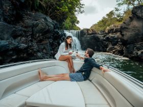 A couple enjoys a romantic moment on a boat, toasting with champagne near a stunning waterfall — an ideal setting for special celebrations or intimate getaways.