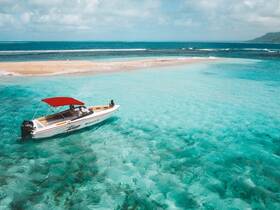 A stunning aerial view of a speedboat anchored in crystal-clear waters near a sandy beach, perfect for exploring tropical destinations.