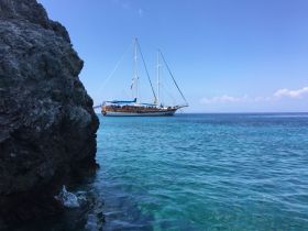 A stunning sailboat anchored in crystal-clear turquoise waters, framed by rocky shores — perfect for scenic boat tours and relaxation.