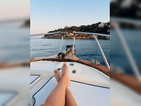 A serene moment on a boat with feet resting on the deck, showcasing the tranquil waters and scenic coastline in the background — perfect for relaxation and enjoying the beauty of nature.