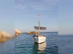 A picturesque view of a classic boat anchored in serene waters, showcasing its elegant design against a backdrop of rocky formations.