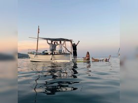 A joyful group celebrates on a boat at sunset, with some enjoying the water — a perfect moment for fun and relaxation on the water.