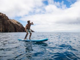 A man paddleboards in clear waters near stunning rocky cliffs, showcasing an adventurous on-water experience perfect for outdoor enthusiasts.