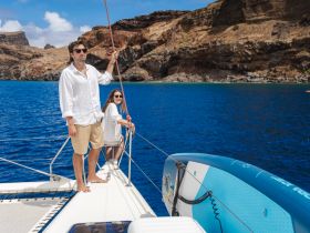 A couple enjoys a sunny day sailing on a catamaran, surrounded by stunning coastal scenery — perfect for romantic getaways or adventure trips.