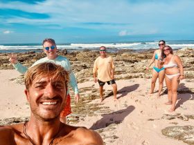A cheerful group poses for a selfie on the beach, capturing a fun moment by the ocean — perfect for memorable vacation experiences.