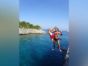 Two friends joyfully leap into the crystal-clear waters from a rocky ledge, capturing the essence of summer fun and adventure by the beach.