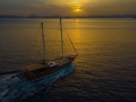 A stunning aerial view of a yacht sailing through calm waters at sunset, showcasing the beauty of maritime adventures.