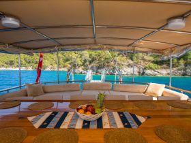 A beautifully arranged dining area inside a boat, featuring a wooden table with a fruit basket and comfortable seating, perfect for enjoying meals while cruising on the water.