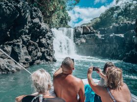 A group enjoys a scenic boat tour, capturing the stunning waterfall backdrop with their cameras — a perfect adventure for nature lovers.