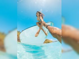 A joyful girl reaches out from the edge of a boat, enjoying a sunny day in crystal-clear turquoise waters — a perfect moment of fun and adventure on the water.