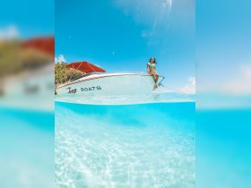 A woman enjoys the sun while perched on the edge of a boat in crystal-clear waters, capturing the essence of a perfect tropical getaway.