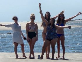A lively group of friends poses joyfully at the beach, capturing a moment of fun and celebration under the sun.