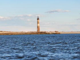 A picturesque view of a historic lighthouse standing tall against a clear blue sky, surrounded by tranquil waters — a perfect landmark for boating adventures.