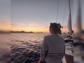 A woman enjoys a stunning sunset view from the deck of a sailboat, creating a perfect backdrop for relaxation and scenic experiences on the water.