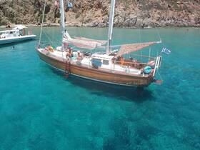 A lively group enjoys a sunny day on a wooden sailboat in the crystal-clear waters of Greece, perfect for swimming and relaxation.