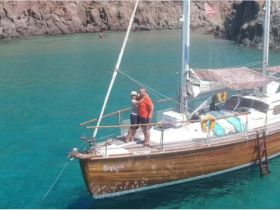 A couple enjoys a moment aboard their sailboat in crystal-clear waters, perfect for romantic getaways and sailing adventures.