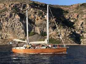 A lively group enjoys a sailing adventure on a beautiful wooden boat, with stunning coastal scenery in the background — perfect for memorable outings on the water.