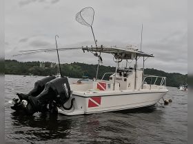 A well-equipped center console fishing boat is docked on calm waters, showcasing its dual Suzuki engines and fishing gear, ideal for a day out on the water.