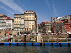 A vibrant waterfront scene showcasing colorful buildings and a lively crowd along the riverbank, perfect for exploring the charm of Porto.