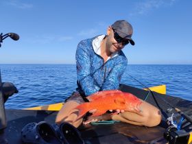 An angler proudly displays a vibrant catch while fishing in open waters, showcasing the thrill of a successful day on the sea.