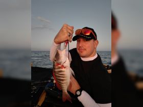 A proud angler holds up his catch against a stunning sunset backdrop, showcasing the thrill of fishing on the open water.