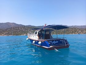 A scenic view of a boat named 'Ayla' cruising through crystal-clear waters, surrounded by beautiful coastal landscapes.