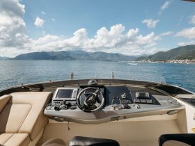 A well-equipped helm of a luxury yacht, showcasing the console and seating area, with stunning views of the mountains and water in the background.