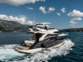 A sleek yacht cruises through clear waters, showcasing its elegant design against a stunning mountainous backdrop — perfect for luxury boating experiences.