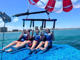 Three friends enjoy an exhilarating parasailing adventure over the ocean, capturing the thrill of water sports and stunning coastal views.