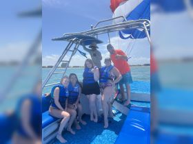 A lively group of friends poses for a photo aboard a boat, ready for an exciting parasailing adventure. The vibrant atmosphere and life jackets highlight the fun and safety of their water activities.