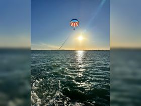 Two people enjoy an exhilarating parasailing experience against a stunning sunset backdrop, capturing the thrill of water sports.