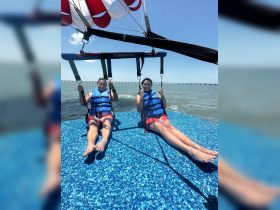 Two friends enjoy an exhilarating parasailing adventure over the water, capturing the thrill of on-water activities and the beauty of the open sky.