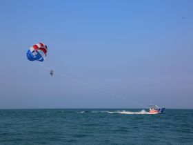 Thrilling parasailing adventure over the ocean, with participants soaring high above the waves, showcasing the excitement of water sports.