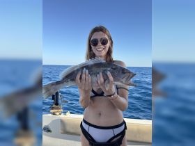 A joyful angler proudly displays her catch while fishing in the open ocean, showcasing the thrill of a successful day on the water.