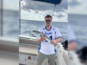 A proud angler displays his catch aboard a boat, showcasing the thrill of fishing on the open ocean.