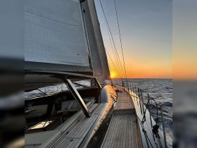 A stunning view of a sleek sailboat under full sail at sunset, showcasing the beauty of sailing on open waters.