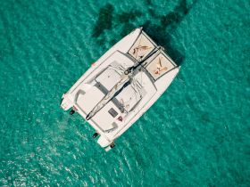 Aerial view of a catamaran with guests lounging on the deck, surrounded by crystal-clear turquoise waters — an ideal setting for relaxation and fun on the water.