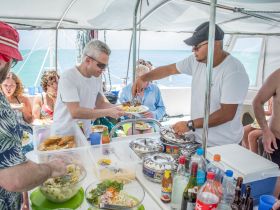 Guests enjoy a delicious meal aboard the boat, showcasing a vibrant dining experience with a variety of dishes and drinks — perfect for group outings on the water.